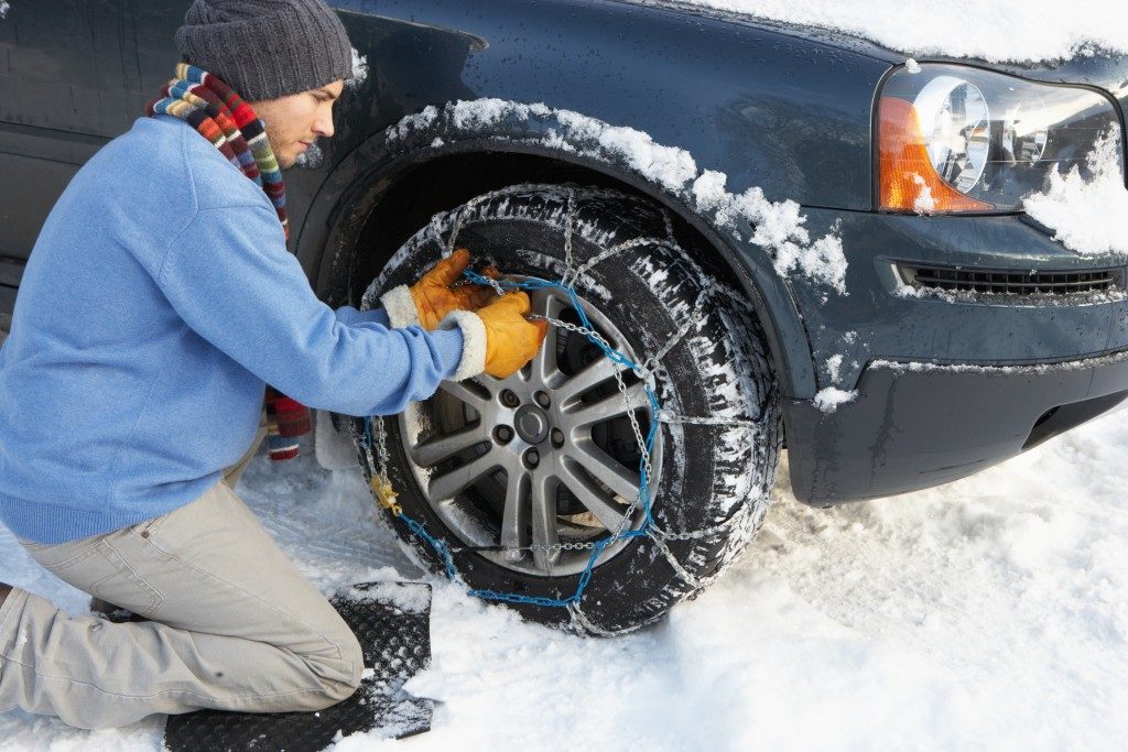 Man Putting Snow Chains Onto Tire Of Car