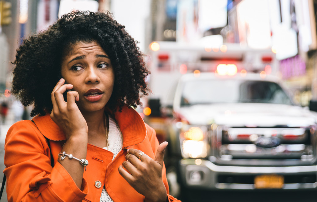 Woman makes a call with an ambulance behind her while in the city