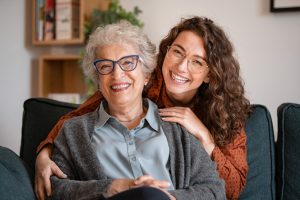 Happy young woman with eyeglasses hugging from behind older grandma