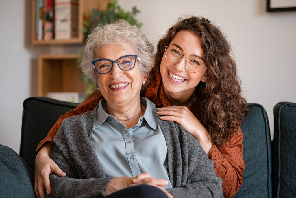 Happy young woman with eyeglasses hugging from behind older grandma